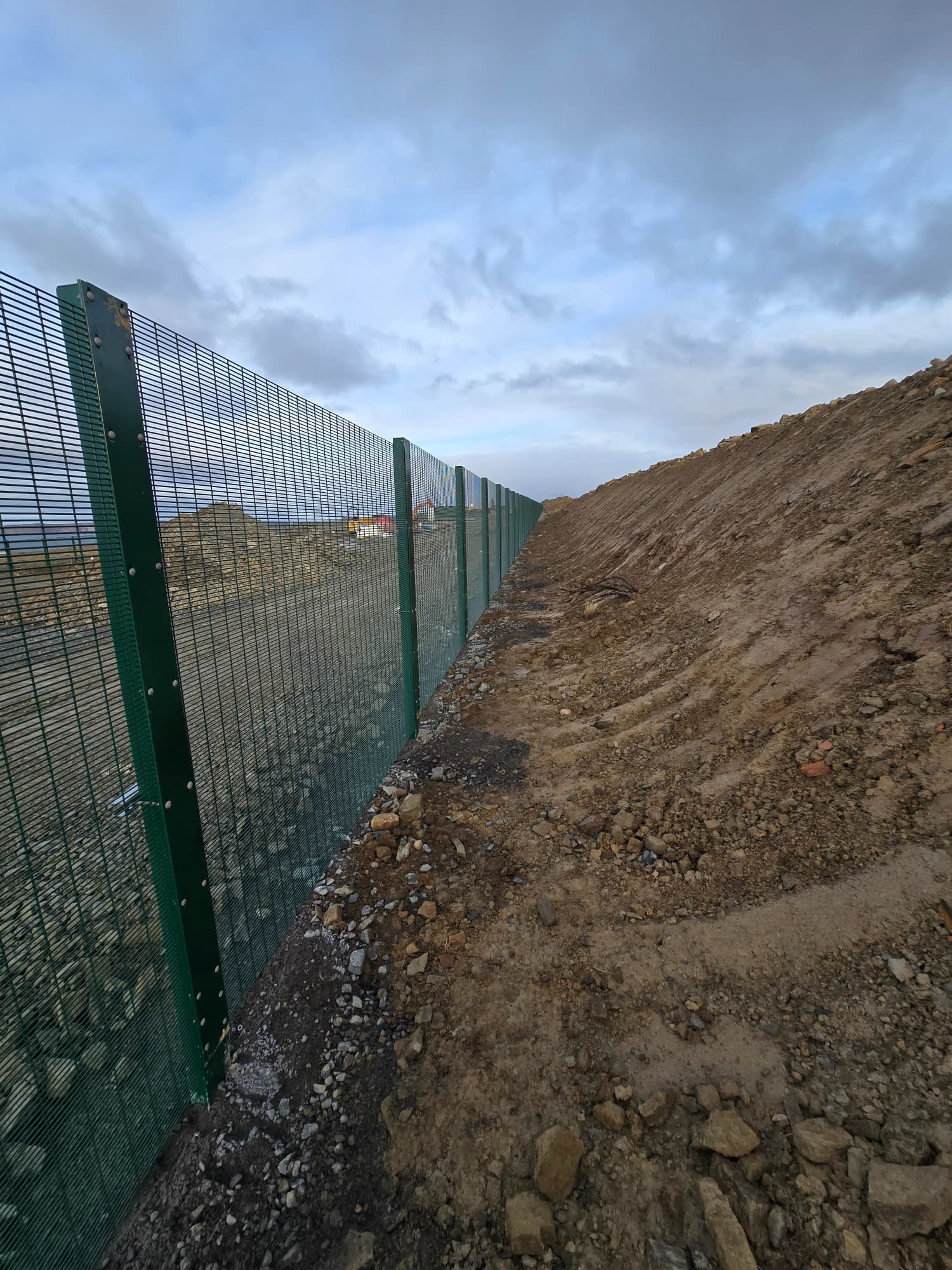 Security mesh following an excavated bank — posts set true on uneven, newly formed ground.