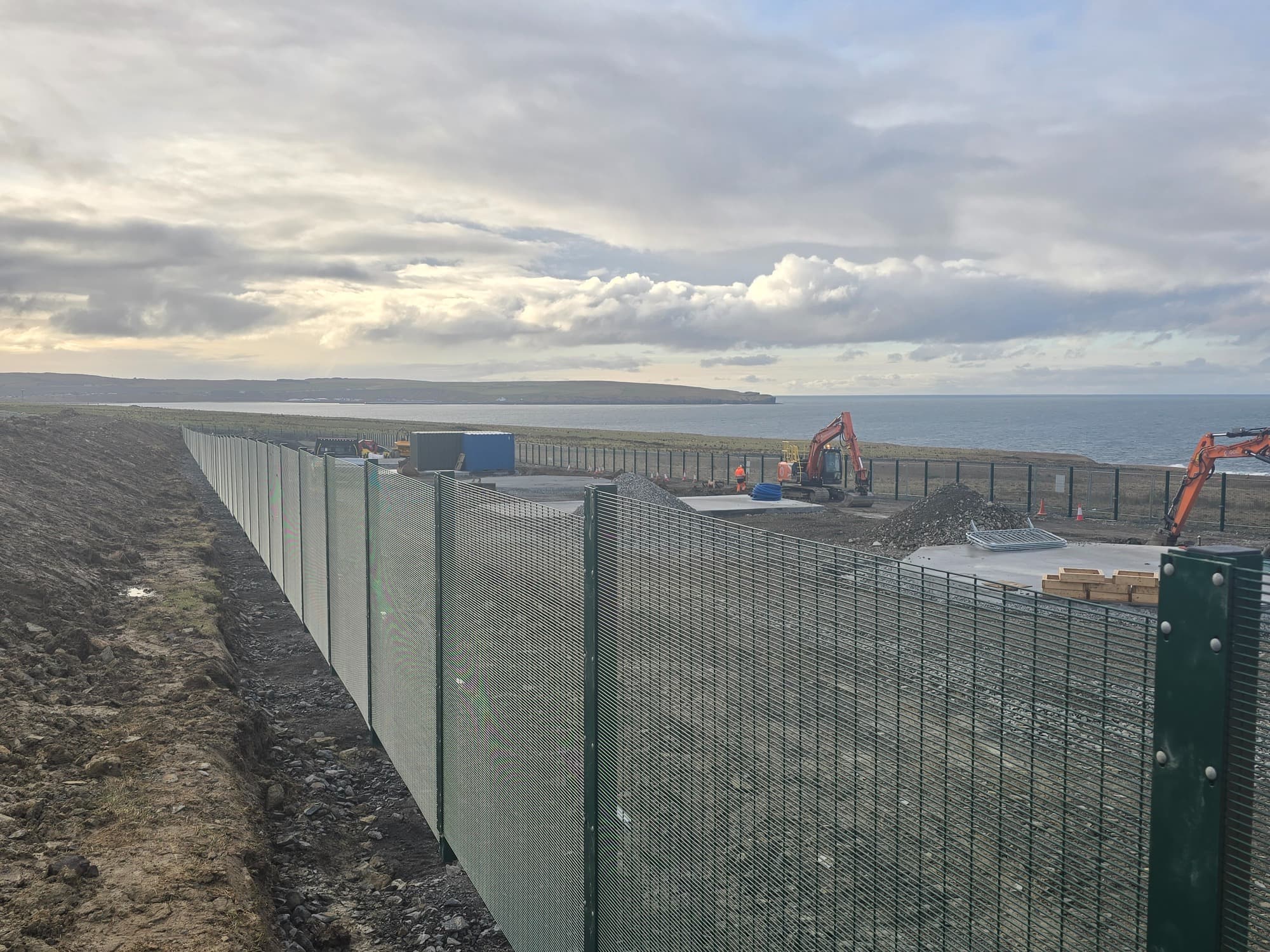 A straight, high mesh perimeter on open ground, showing the scale of a specialist site job.