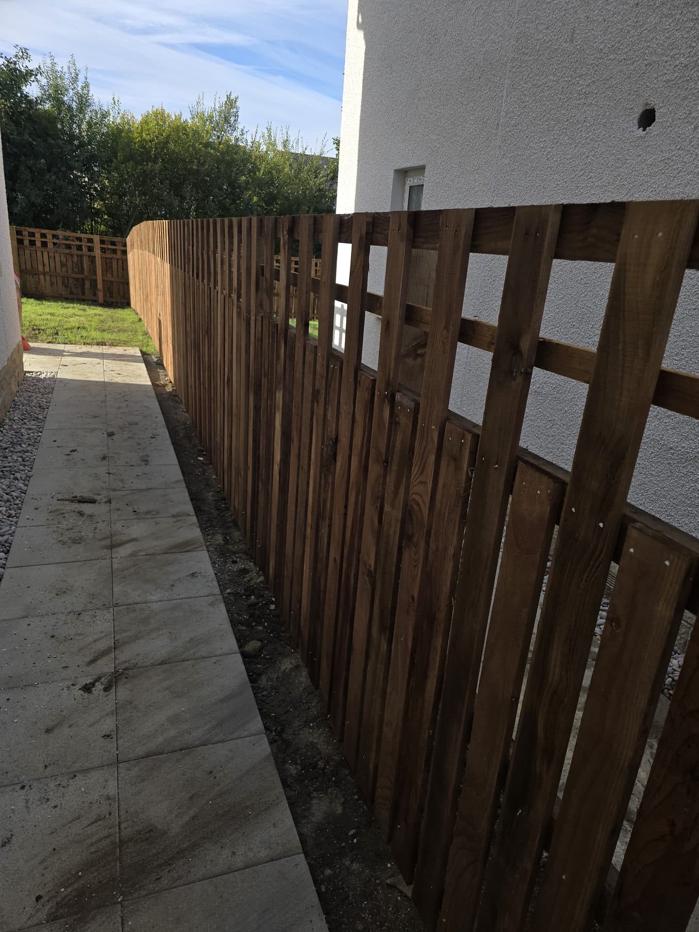 Finished dark-stained hit-and-miss timber fence along a house path in East Calder